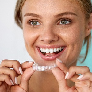 A smiling woman holding a teeth whitening tray near her face