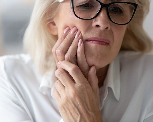 Senior woman with glasses rubbing jaw in pain